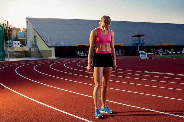 Picture of beautiful young european female runner or sprinter standing on outdoor stadium track feel...