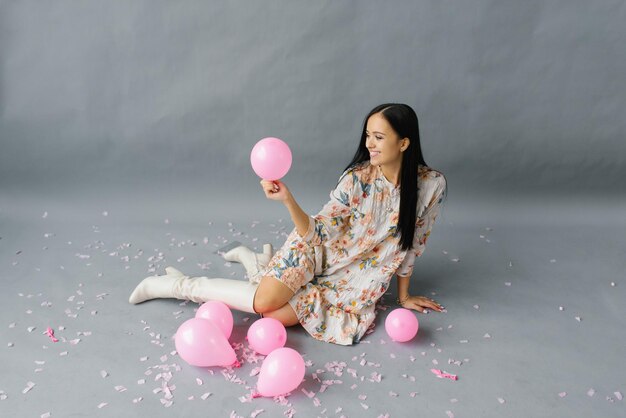 A picture of a cheerful woman who feels very happy, holding a pink balloon and laughing, posing near balloons