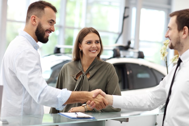 Picture of confident young salesman explaining all the car features to the young attractive owners