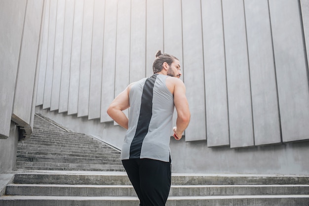 Picture of dark-haired young man jogging up on stairs. He looks to right. Guy wears sports uniform. He is strong and well-built.