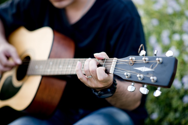 Picture of a guitarist, a young man playing a guitar while sitting in a natural garden,music concept