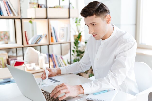 Picture of handsome man dressed in white shirt using laptop computer. Coworking. Looking at computer.