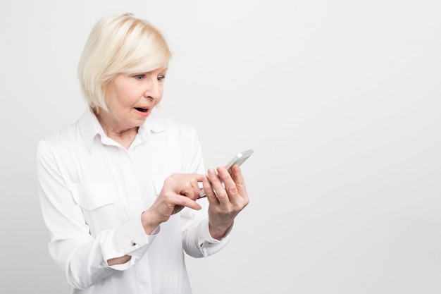 A picture of old lady holding new smartphone. She doesn't know how to use it properly because she didn't have anything like this phone before.