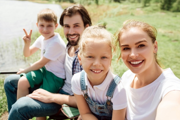 A picture of one family sitting together at the edge of riveer shore. They are looking straight and smiling. Boy is showing piece symbol.