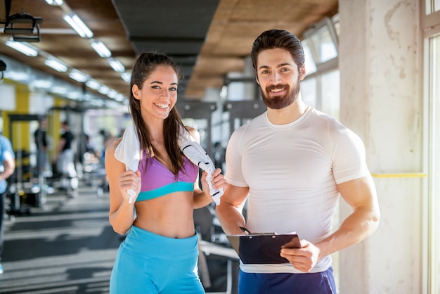 Picture of personal fitness trainer and his female client in gym posing in front of the camera.