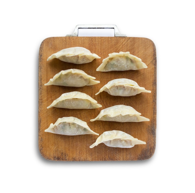 Picture of raw dumplings or gyozas on wooden cutting board isolated on white background