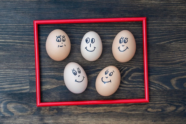 Picture red frame and many funny eggs smiling on wooden wall background closeup Eggs family emotion face portrait Concept funny food