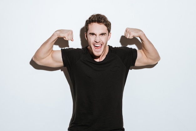 Picture of screaming young man dressed in black t-shirt posing over white background looking at camera. Showing biceps.