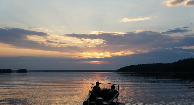 Picture of sunset on lake with floating boat and people