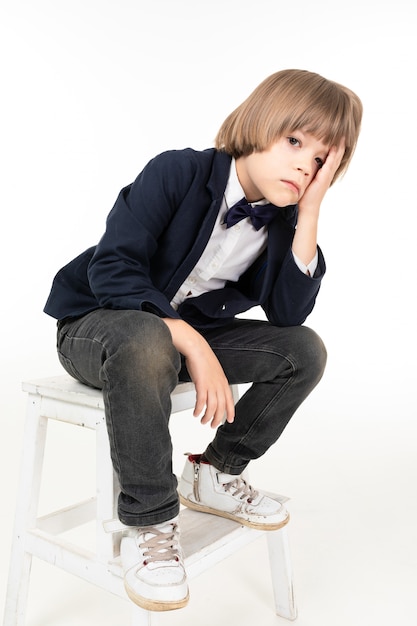 Picture of a teenager boy in black suit and white sneakers sits on his knees and not happy isolated