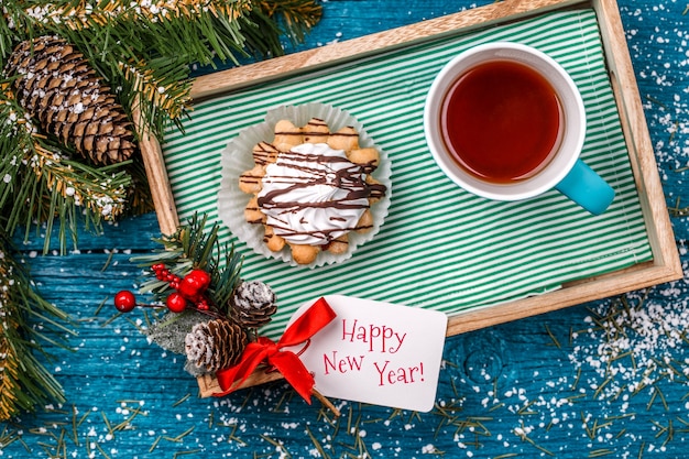 Picture of tray with mug of tea and cakes on table with spruce branches, snow and Christmas decoration, postcard