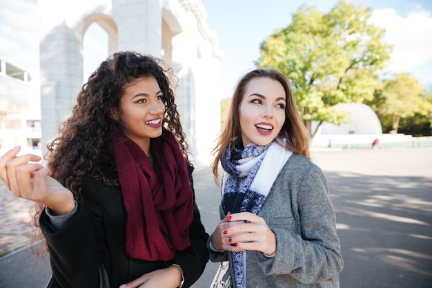 Picture of two beautiful young women wearing scarfs communication and look aside.