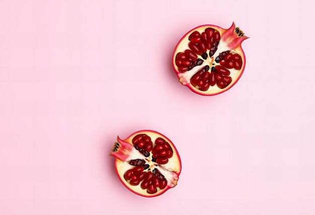 Photo picture two pomegranate halves on a pink background in minimalist flat lay top view