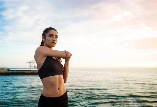 Picture of young beautiful fitness girl who makes sport exercises with sea on