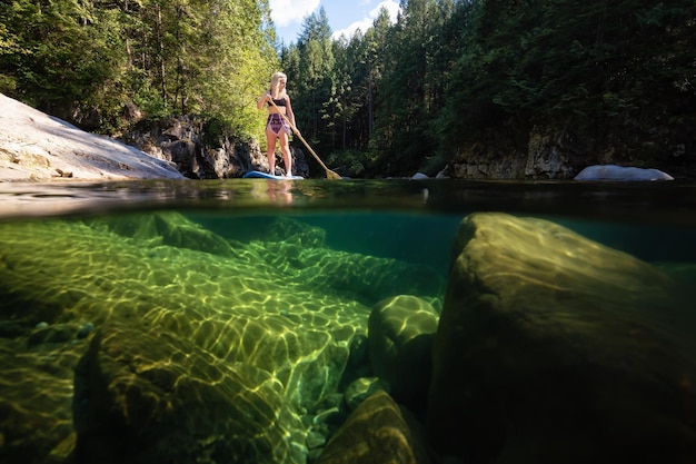 Over and Under Picture of a young Caucasian girl paddle boarding in a river