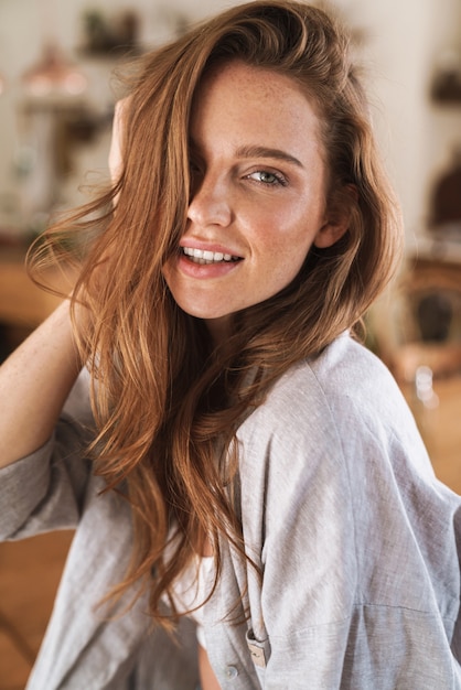 Picture of young cheerful beautiful optimistic happy pleased redhead woman indoors at home.