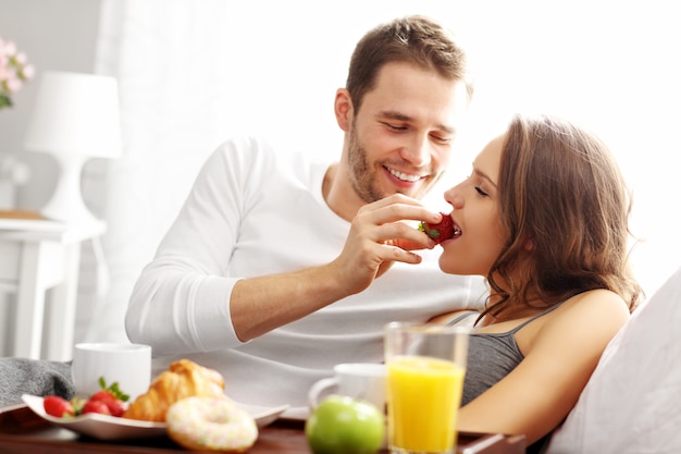 Picture of young couple eating breakfast in bed