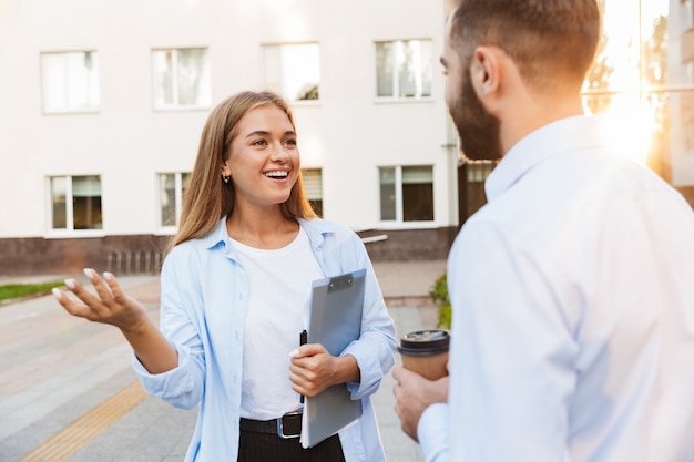 Picture of a young emotional happy pleased man and woman businesspeople outside at the street near business center talking with each other.