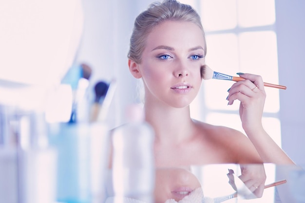 A picture of a young woman applying face powder in the bathroom