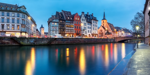 Picturesque panorama of quay and church of Saint Nicolas with mirror reflections in the river Ile during evening blue hour, Strasbourg, Alsace, France