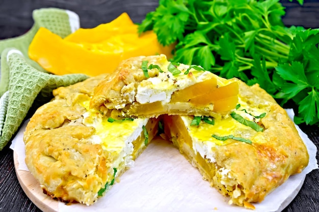 Pie of pumpkin salty feta cheese egg cream and herbs green napkin basil and parsley on a background of wooden boards