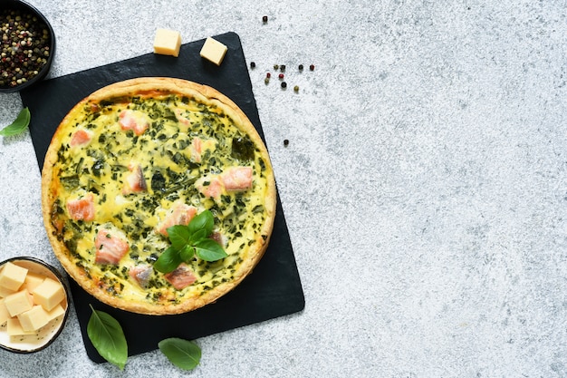 Pie (quiche) with salmon, spinach and cheese on a stone board on a concrete.