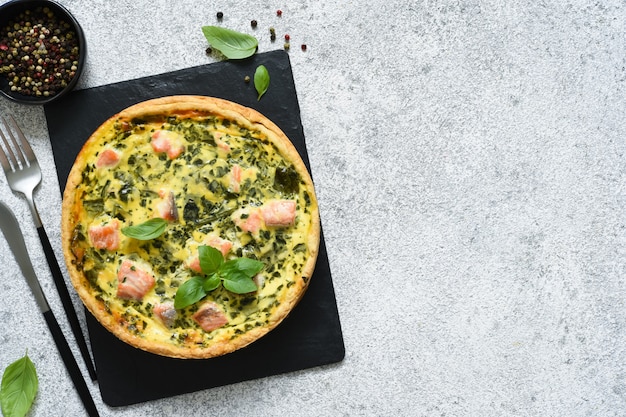 Pie (quiche) with salmon, spinach and cheese on a stone board on a concrete.