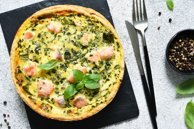 Pie (quiche) with salmon, spinach and cheese on a stone board on a concrete.