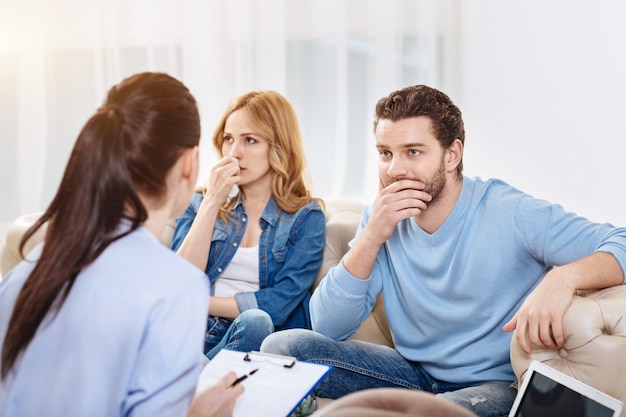 Piece of advice. Thoughtful pleasant young man holding his chin and listening to the psychologist while discussing the problem