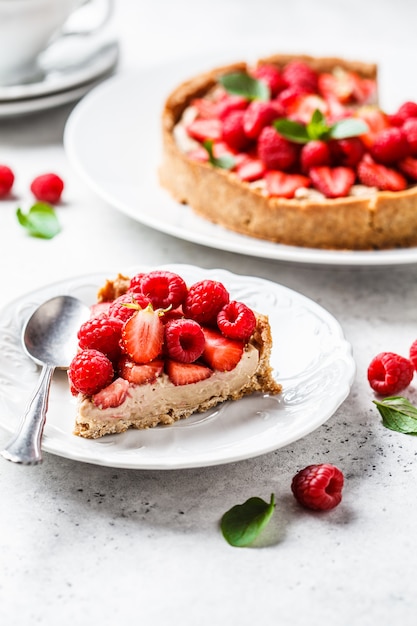 Piece of berry tart with raspberries, strawberries and cream on white plate