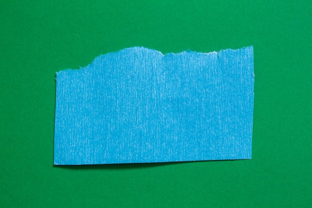 A piece of blue paper is torn off on a green background.