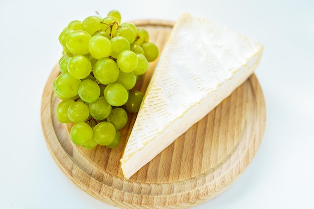 piece of brie cheese, white grapes on wooden round cutting board. Side view, close-up