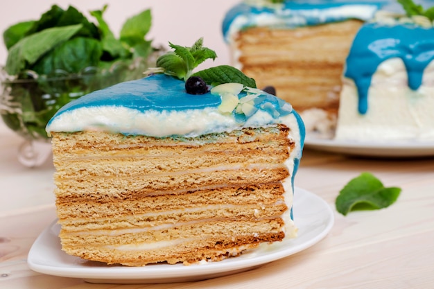 Piece of cake decorated with blue cream, mint and blueberries on a wooden table.