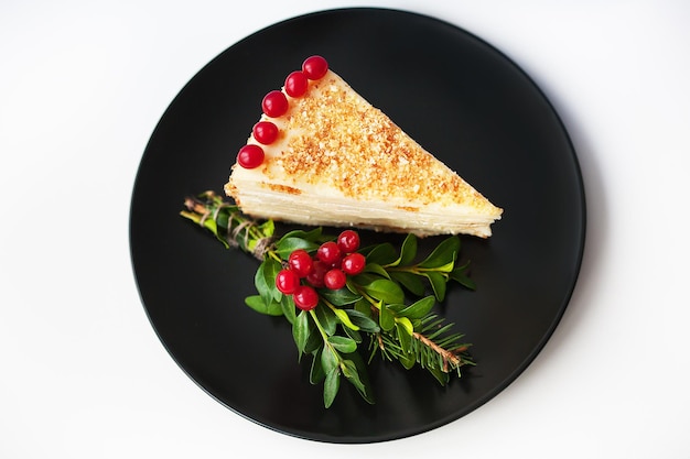 Piece of cake decorated with tree branches and berries viburnum on a black plate.