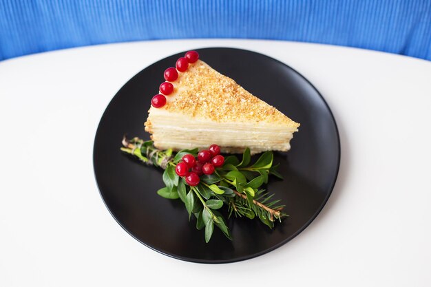 Piece of cake decorated with tree branches and berries viburnum on a black plate