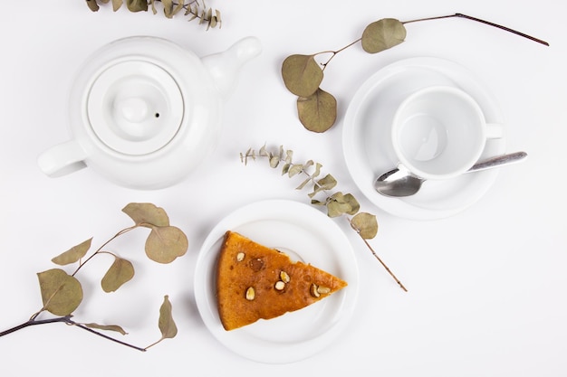 A piece of cake on a saucer with a cup for tea or coffee and a kettle