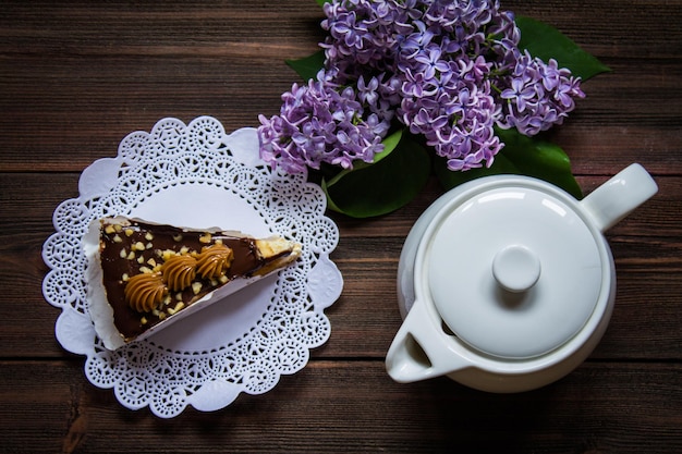 Piece of cake teapot and lilac on a brown wooden background