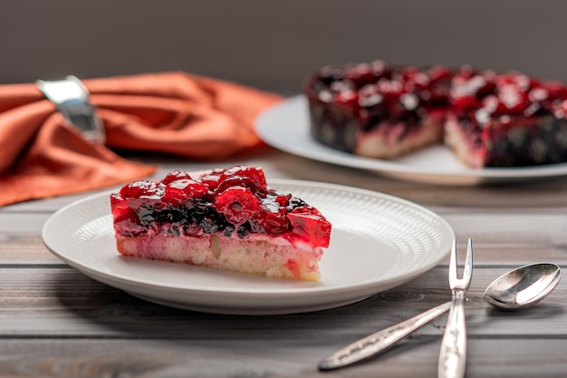 Piece of cake with berries raspberry currant strawberry on a white plate next to dessert spoon and