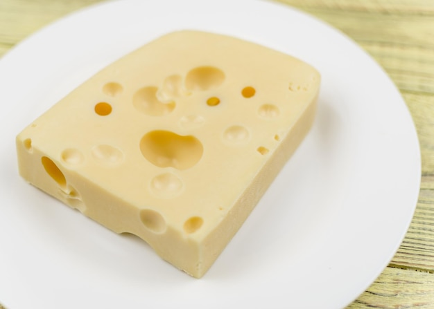 A piece of cheese with holes and a knife for cutting on a white plate