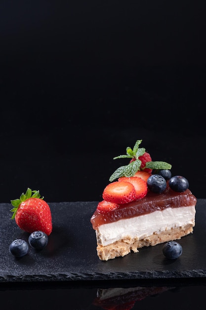 Piece of cheesecake isolated  served on slate plate on black background with copyspace. Vertical format. Homemade bakery concept.