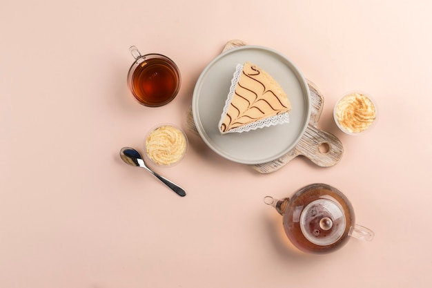 A piece of cheesecake on a plate with a teapot and a cup of tea