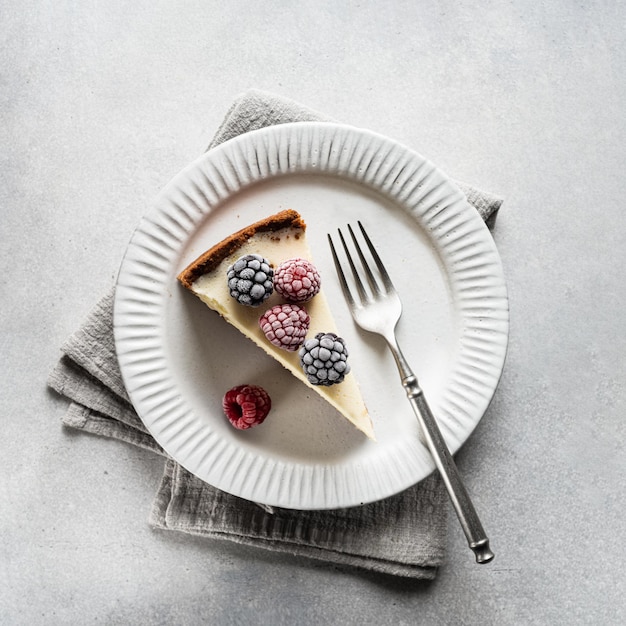 A piece of cheesecake with frozen berries on a white ceramic plate on a concrete background top view