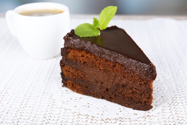 Piece of chocolate cake on plate and cup of coffee on napkin on fabric background