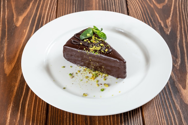 Piece of chocolate cake with pistachios and mint leaves on white plate