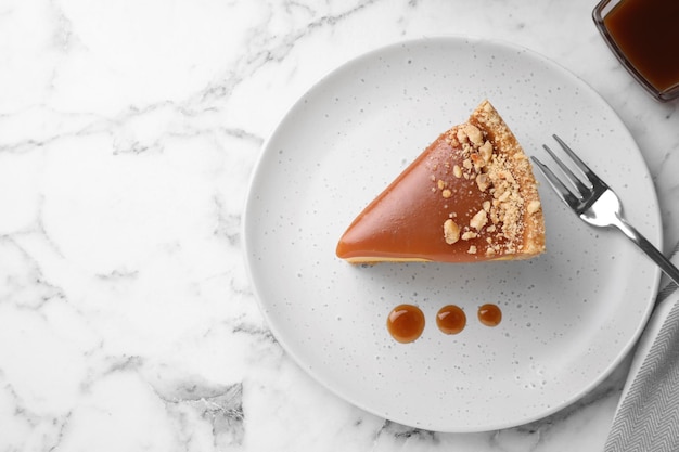 Piece of delicious cake with caramel served on white marble table flat lay Space for text