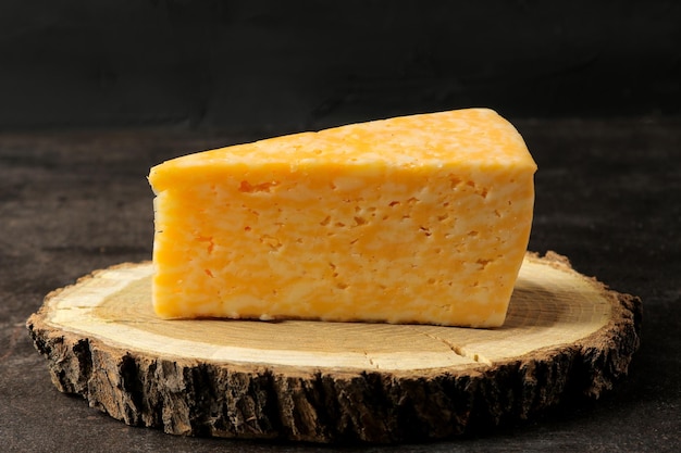 A piece of delicious marbled cheese on a wooden stand against a dark background. close-up