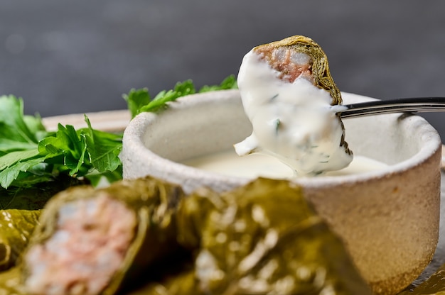 Piece of dolma with sour cream on black fork over the saucepan selective focus macro