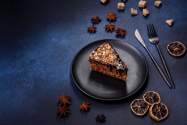 A piece of fresh delicious cake with nuts and chocolate on a black plate against a dark blue background