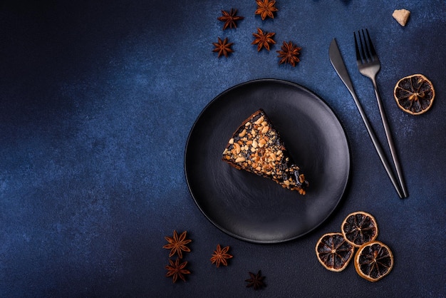 A piece of fresh delicious cake with nuts and chocolate on a black plate against a dark blue background