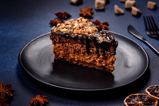 A piece of fresh delicious cake with nuts and chocolate on a black plate against a dark blue background